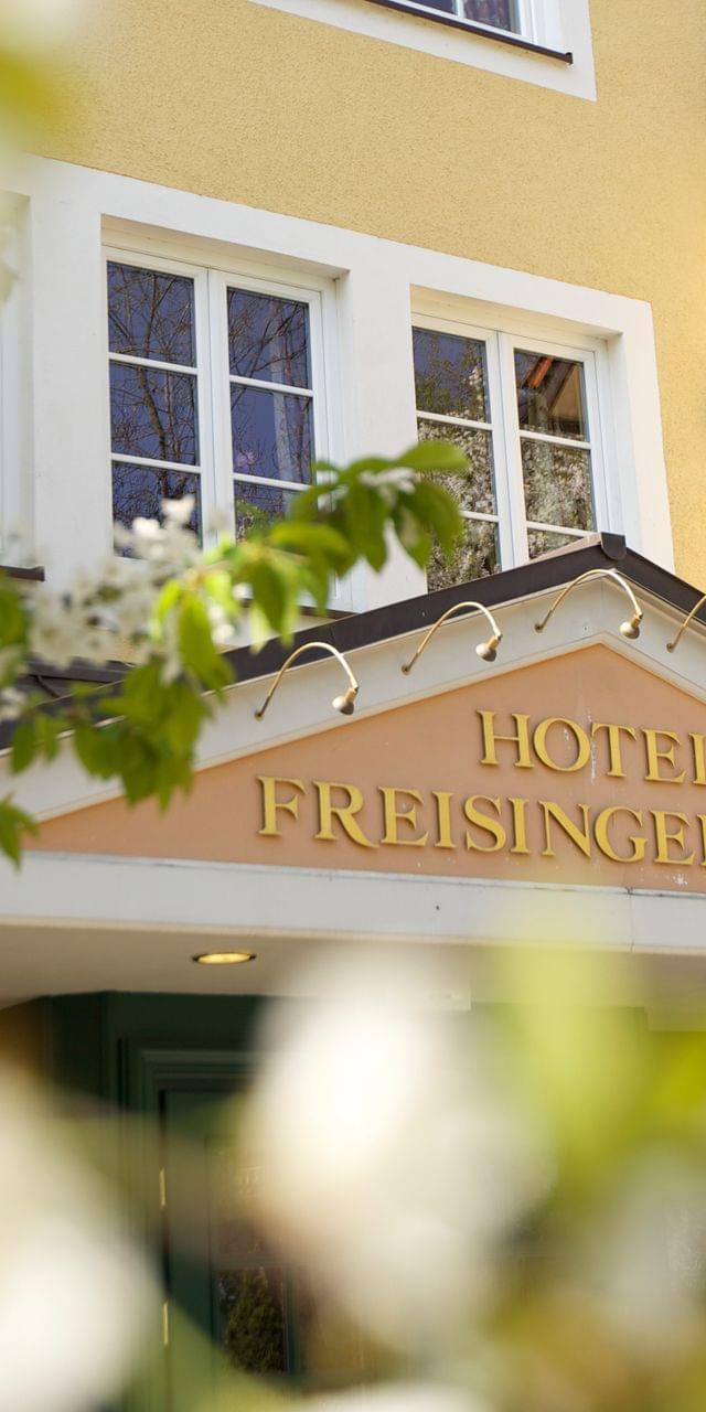 Close-up of the lettering Freisinger Hof above the entrance door and the yellow facade above it.