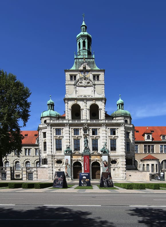 Außenansicht des Bayerischen Nationalmuseums München mit seiner historistischen Fassade und dem markanten Turm vor blauem Himmel.