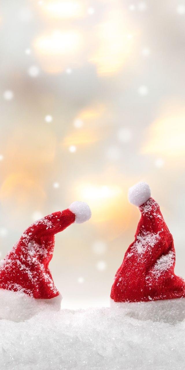 Vier kleine rote Weihnachtsmützen im Schnee vor unscharfen Lichtern im Hintergrund – stimmungsvolle Weihnachtsdekoration für die Adventszeit.