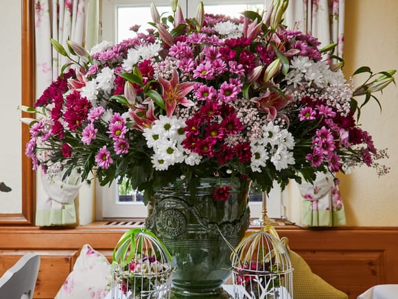 Lush floral arrangement in a green glass vase featuring pink, white, and deep red blooms.