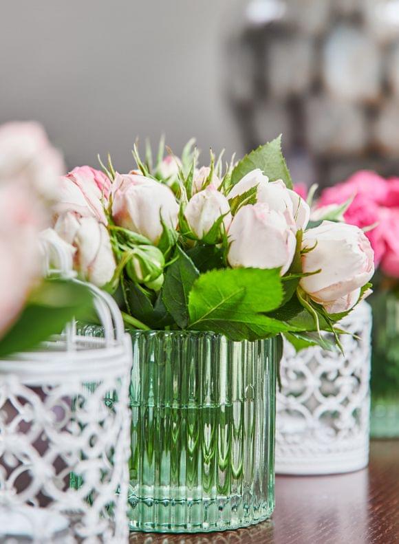 Kleine Blumenvasen aus grünem Glas mit rosa und pinken blumen und weißen kleinen Vogelkäfigen dazwischen in einer Reihe.