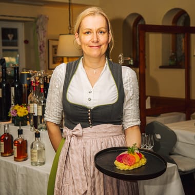 Servicemitarbeiterin in Dirndl serviert ein ansprechend angerichtetes Gericht im Restaurant Freisinger Hof.