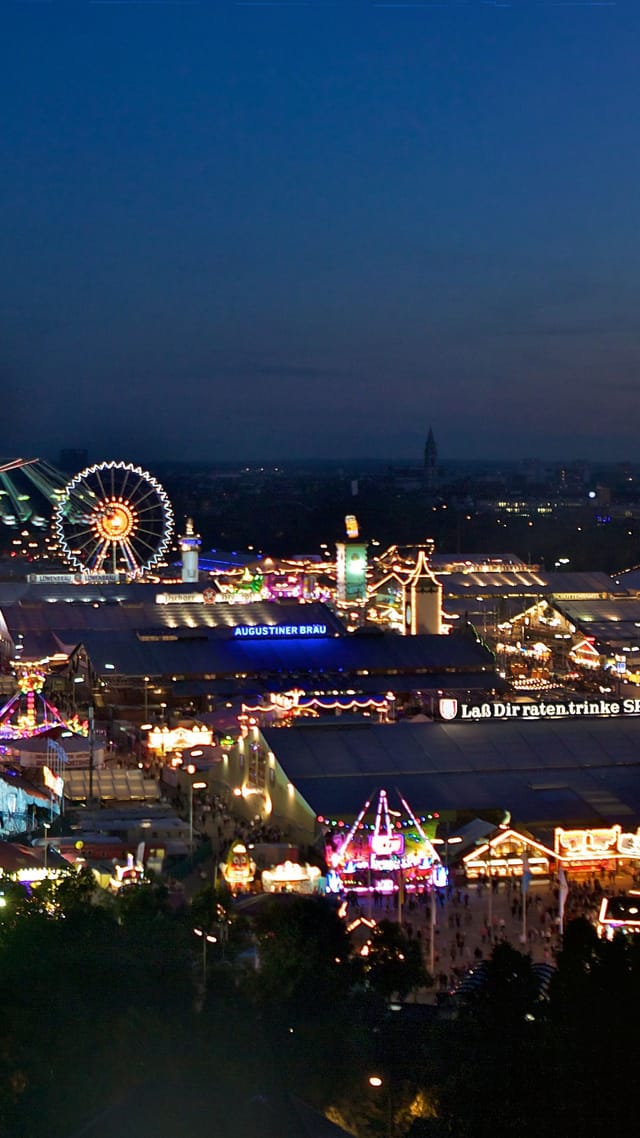 Weitläufiger Blick über die hell erleuchtete Theresienwiese beim Münchner Oktoberfest zur blauen Stunde.