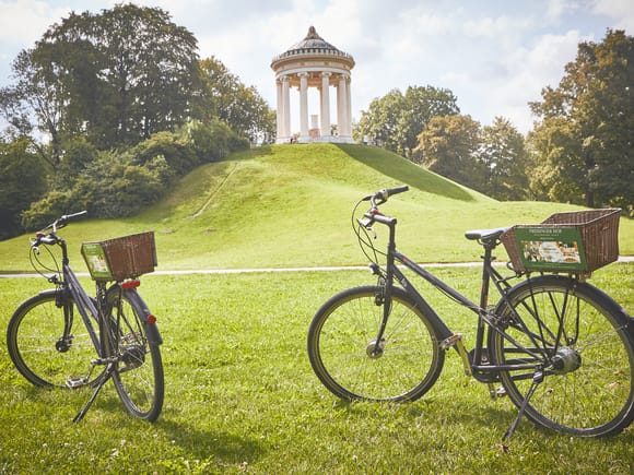 Two bicycles on a green meadow in front of a small temple on a hill.