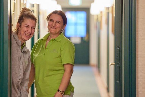 Zwei fröhlich lächelnde Mitarbeiterinnen des Housekeeping-Teams stehen im Flur des Hotels.