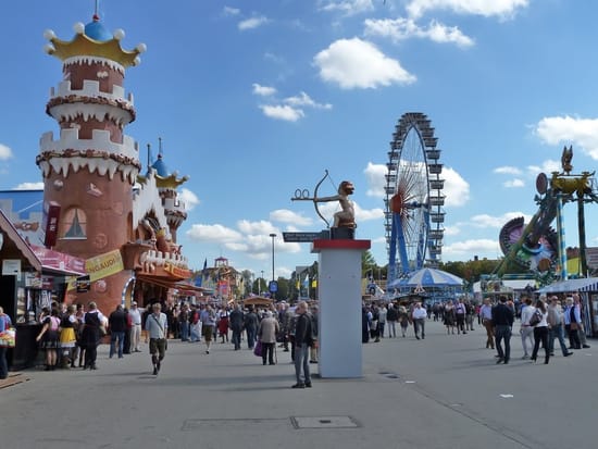 Festplatz eines großen Volksfests mit Fahrgeschäften, Türmen und Riesenrad bei blauem Himmel.