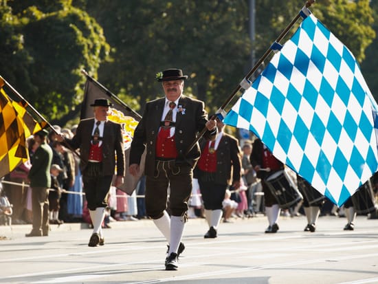 Trachten- und Schützenzug beim Münchner Oktoberfest, Teilnehmer in traditioneller bayerischer Tracht tragen die blau-weiße Rautenflagge.
