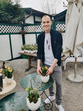 Service employee decorating the terrace with spring floral arrangements in white flower pots shaped like eggshells.
