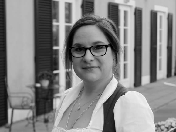 Black and white photograph of a female hotel employee in a dirndl in front of the hotel terrace.