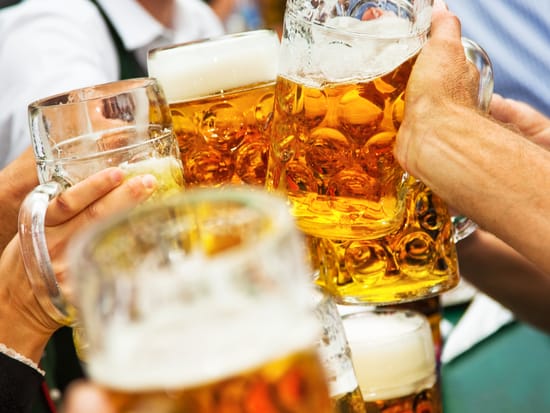 Mehrere Personen stoßen mit großen Bierkrügen auf einem Volksfest an.