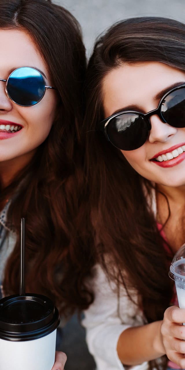 Two young women wearing sunglasses laughing and taking a selfie – carefree time with friends and city trip vibes.