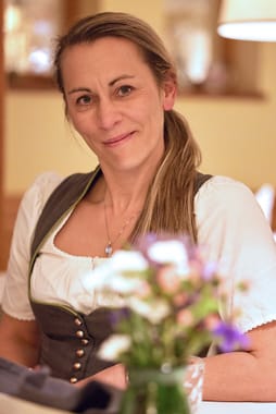 Freundlich lächelnde Servicemitarbeiterin beim Eindecken des Restaurants, im Vordergrund ein frischer Blumenstrauß.