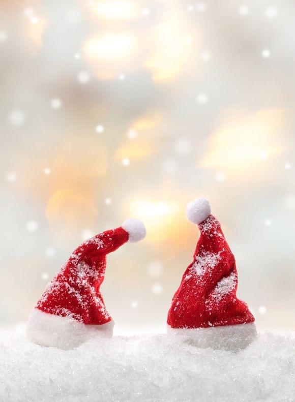 Vier kleine rote Weihnachtsmützen im Schnee vor unscharfen Lichtern im Hintergrund – stimmungsvolle Weihnachtsdekoration für die Adventszeit.
