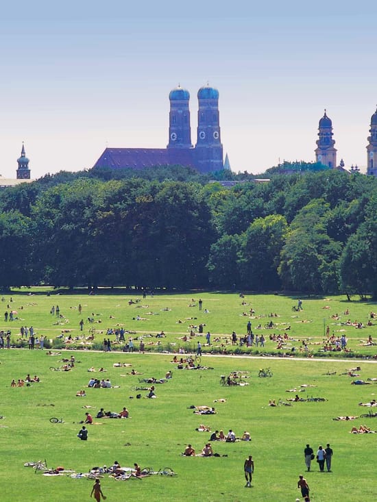 Expansive lawn in Munich's English Garden with a view of the old town skyline, including the towers of the Frauenkirche.