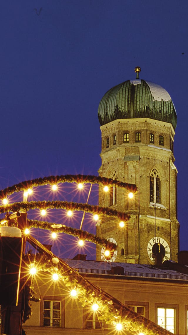 The Mariensäule column on Munich's Marienplatz, festively illuminated, with the towers of the Frauenkirche glowing in the evening light.