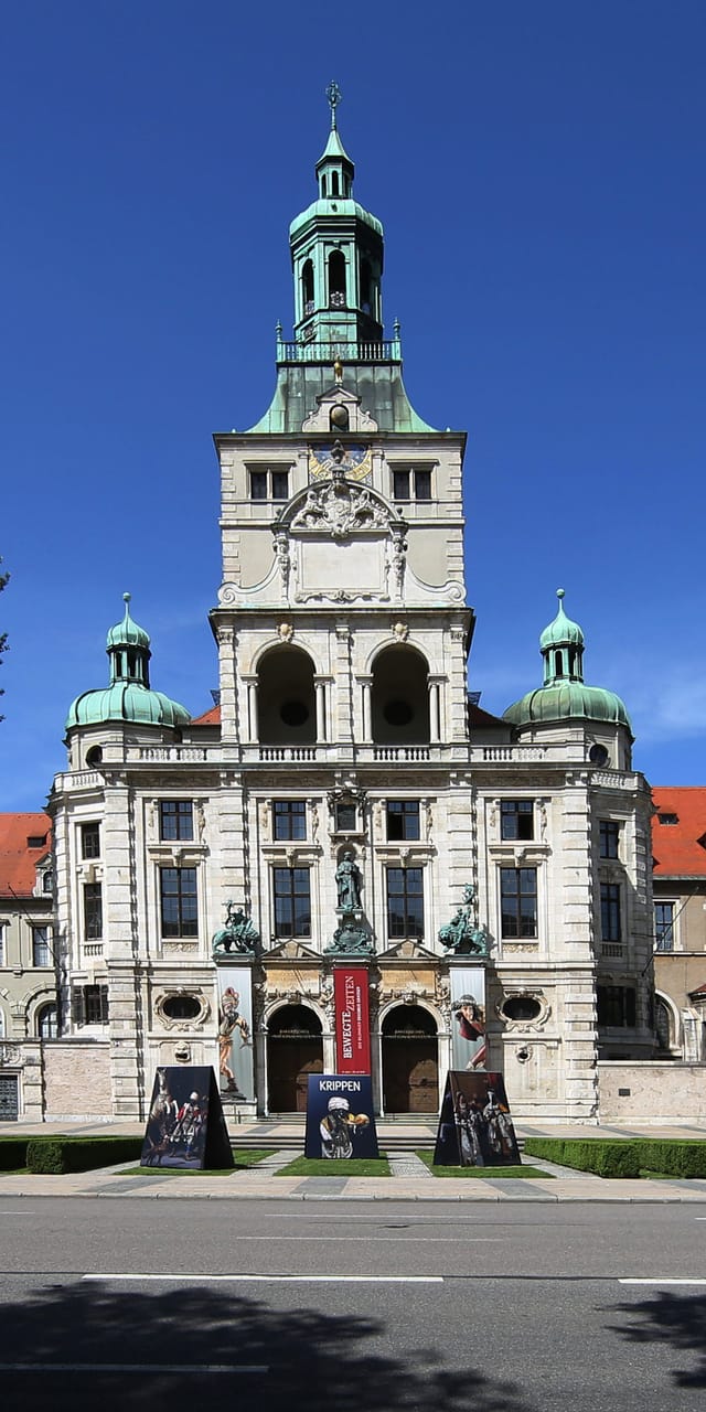 Außenansicht des Bayerischen Nationalmuseums München mit seiner historistischen Fassade und dem markanten Turm vor blauem Himmel.