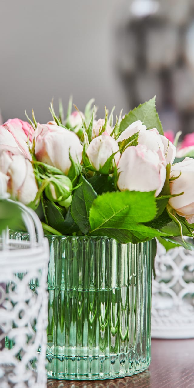 Small flower vases made of green glass with pink and fuchsia flowers and small white bird cages in between, arranged in a row.