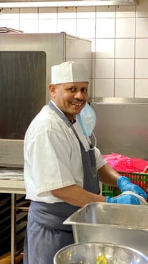 Smiling kitchen employee in white chef's clothing and hat at work in the restaurant kitchen.