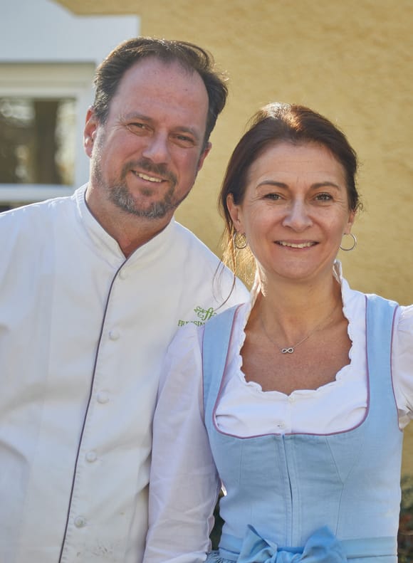 Die Gastgeber des Freisinger Hof München: Küchenchef Karl Wallisch und seine Frau stehen lächelnd vor dem Restaurant.