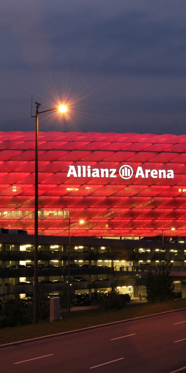 Allianz Arena - Fußballstadion mit rot beleuchteter Fassade bei Dämmerung.