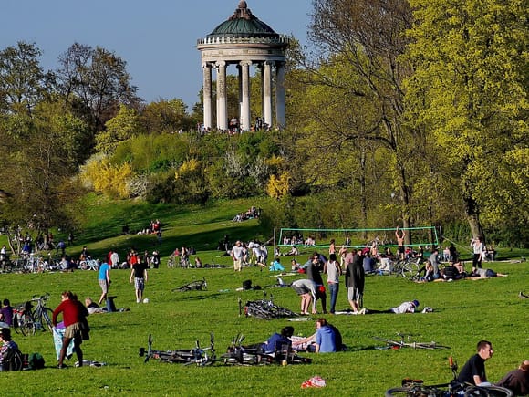 People relaxing on a meadow in Munich's English Garden, the Monopteros visible on its hill in the background.
