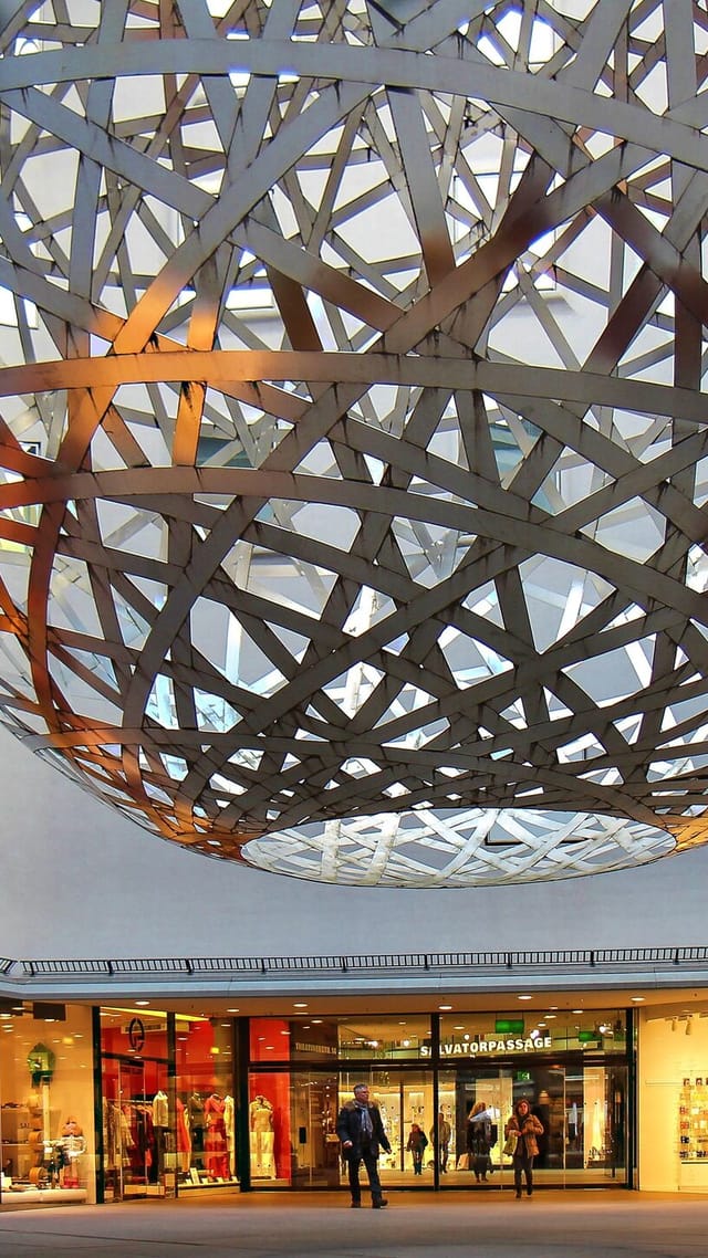 Die Stahlkugel-Sphere von Olafur Eliasson im Viscardihof der Fünf Höfe München, umgeben von Einzelhandelsgeschäften.