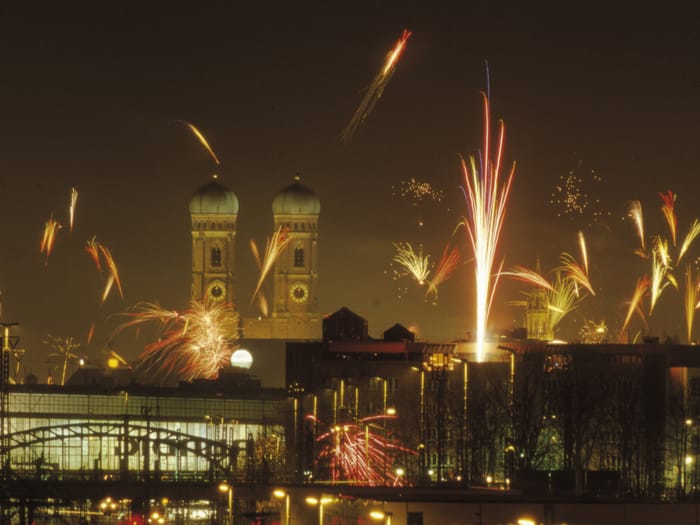Silvesterfeuerwerk erleuchtet den Nachthimmel über München, mit den Türmen der Frauenkirche im Hintergrund.