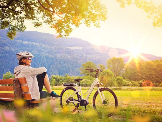 Radfahrer macht Rast auf einer Bank mit Blick auf Berge im Sonnenuntergang.