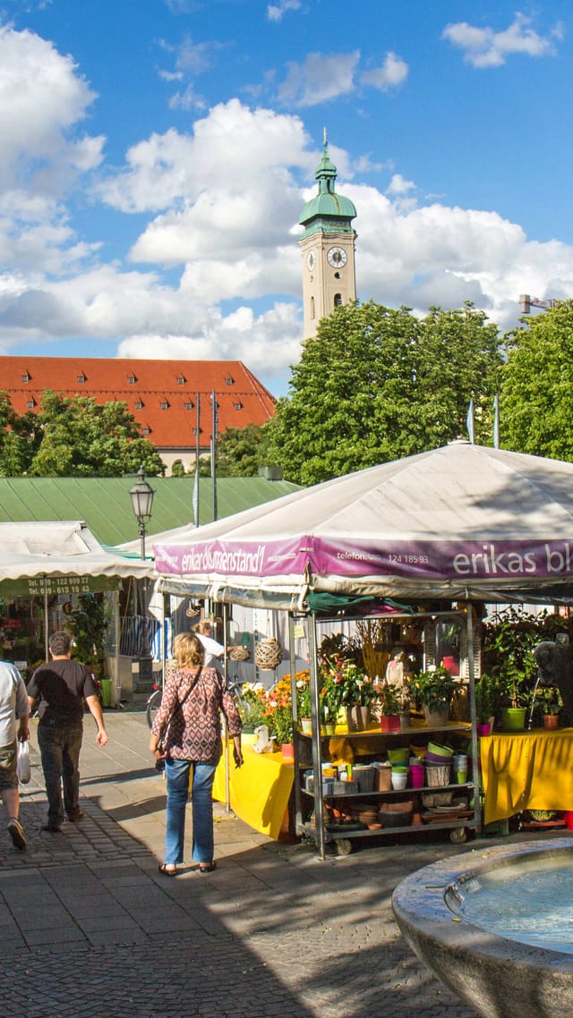 Blumenstände auf dem Viktualienmarkt München, im Hintergrund der bunt bemalte Maibaum und ein Kirchturm.