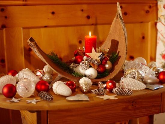 Weihnachtsdeko mit einer roten Kerze in einem Rindenschiff und rotem und weißem Christbaumschmuck.