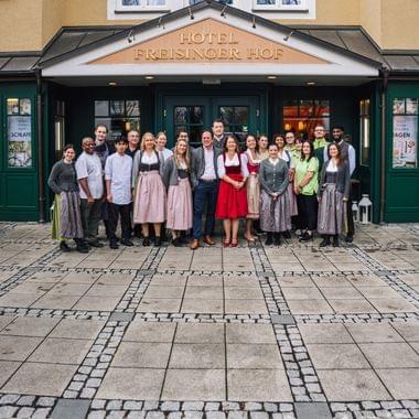 The team of the Hotel and Restaurant Freisinger Hof posing together in front of the hotel entrance — many staff members are dressed in Bavarian traditional costume.