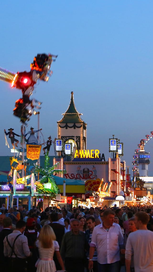 Das Münchner Oktoberfest in der Abenddämmerung, mit beleuchteten Fahrgeschäften, Riesenrad und einer belebten Menschenmenge.