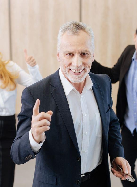 Fünf motivierte Mitarbeiter in Office-Outfit, die die Arme hochwerfen oder den Daumen hoch halten.