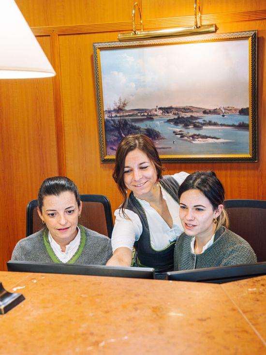 Drei Hotelmitarbeiterinnen arbeiten gemeinsam an einem Computerarbeitsplatz an der Rezpetion des Hotels.