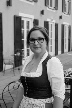 Black and white photograph of a female hotel employee in a dirndl in front of the hotel terrace.