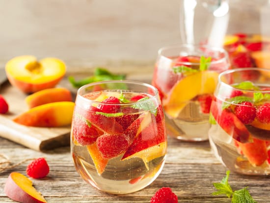 Fruchtiger Sommerpunsch mit Erdbeeren und Pfirsichen in Gläsern auf Holztisch.