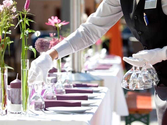 Service staff setting a festively laid table with glasses and flowers.