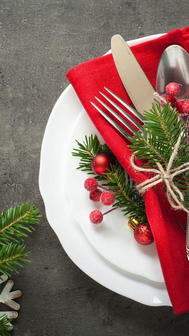 Weihnachtliches Tischgedeck mit roter Serviette, zusammengebundenem Besteck und Tannenzweig-Dekoration auf weißem Teller.