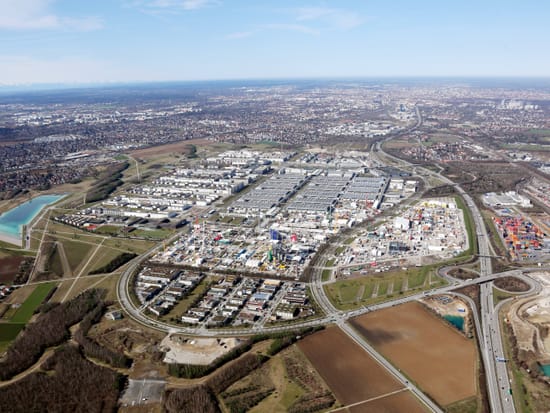 Luftaufnahme eines Münchner Wohnviertels mit Blick auf die Stadt und die Landschaft im Hintergrund.