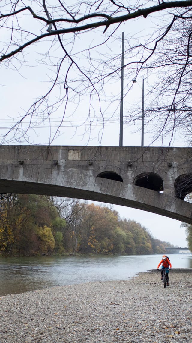 Steinbrücke über einen ruhigen Fluss mit einem Fahrradfahrer am Ufer.