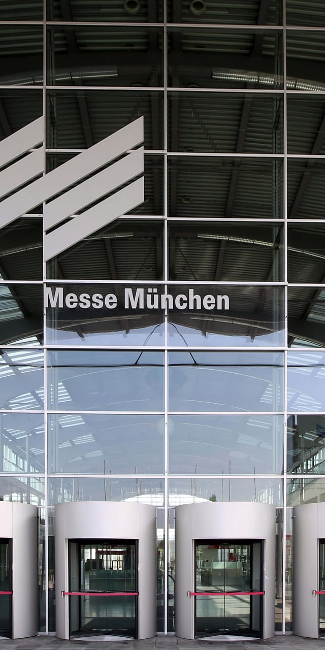 Haupteingang der Messe München mit markanter Glasfassade und den Eingangstüren im Vordergrund.
