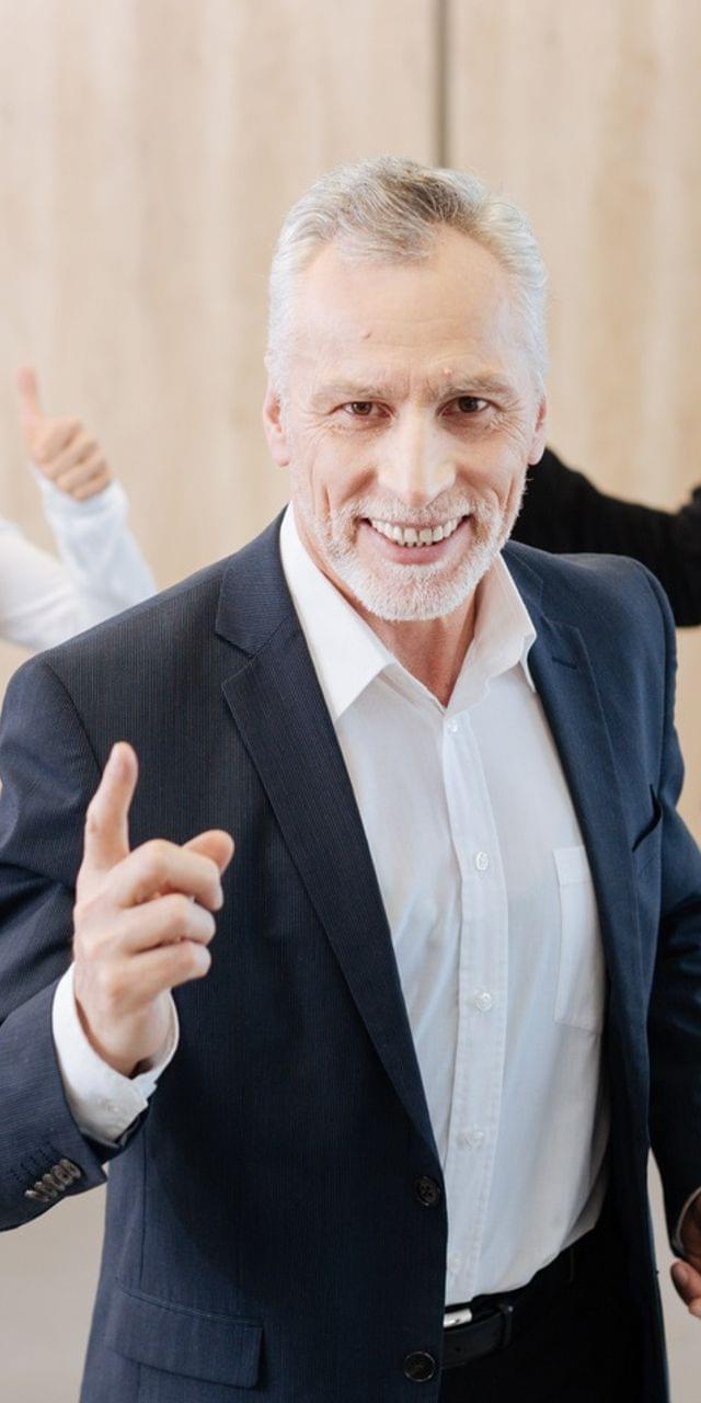 Five motivated employees in office attire throwing their arms in the air or giving a thumbs up.