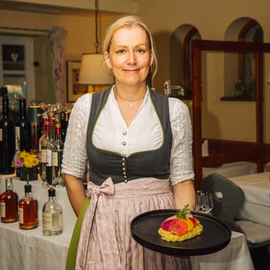 Female service staff member in a dirndl serving an attractively presented dish in the Freisinger Hof restaurant.