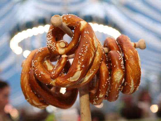 Frisch gebackene Brezn aufgereiht am Ständer, im Hintergrund die typische Bierzeltdekoration des Oktoberfests.